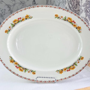 May include: Oval, white serving platter with a floral design. The platter has a red and gold border with a repeating pattern. Yellow and orange flowers with green leaves are arranged in clusters around the rim.