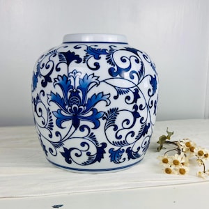 May include: A white and blue ceramic ginger jar with a floral design. The jar features a rounded shape with a wide base and a narrow neck. The blue floral pattern is intricate and covers the entire surface of the jar.