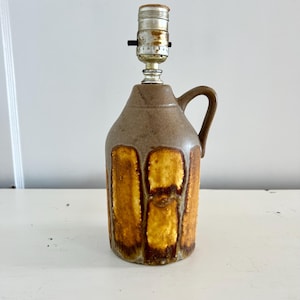 May include: A brown ceramic lamp with a handle and a textured, rectangular pattern in shades of gold and brown. The lamp has a silver lamp holder at the top.