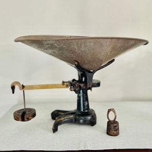 Peut inclure: Balance antique en métal noir et laiton avec un grand plateau rond en métal gris. La balance a trois pieds et un petit poids rond.