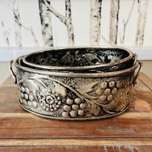 May include: Two silver metal bowls with an embossed grapevine design. The bowls are nested together and have a rustic, vintage look.