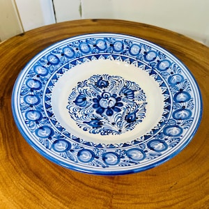 May include: A white ceramic plate with a blue and white floral design. The plate has a raised rim and a scalloped edge.