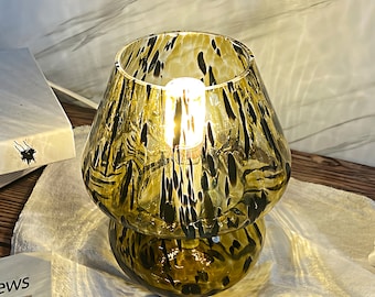 May include: A table lamp with a brown and black patterned glass shade and base. The lamp is turned on and the light bulb is glowing.