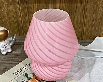 May include: A pink glass table lamp with a swirl design. The lamp has two tiers, with the top tier being larger than the bottom tier.
