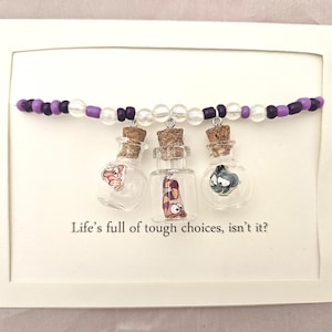 May include: A framed artwork featuring three small glass bottles with cork stoppers, each containing a whimsical illustration. The bottles hang from a beaded strand of purple and clear beads. The text "Life's full of tough choices, isn't it?" is below the bottles.