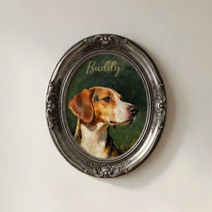 May include: An oval framed portrait of a dog named Buddy. The dog has brown and white fur and is set against a dark green background. The frame is silver with ornate detailing. The word "Buddy" is written in gold script above the dog.