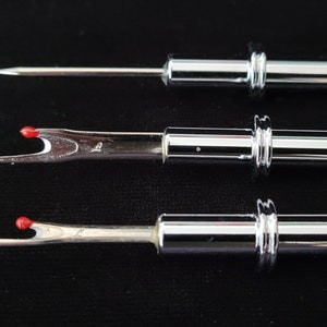 May include: Three silver sewing tools with red tips. The tools are different sizes and have a needle-like point on one end and a small hook on the other end.