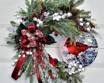 May include: A Christmas wreath with a red cardinal design. The wreath is decorated with red berries, white berries, pine branches, and a red bow with a white snowflake pattern.