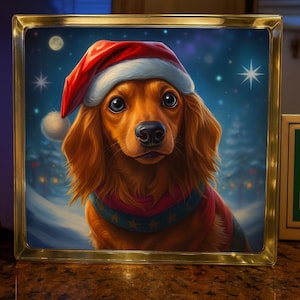 Puede incluir: Una obra de arte navideña enmarcada que representa a un perro salchicha con un gorro de Papá Noel y una bufanda festiva. El perro tiene ojos grandes y expresivos y está ambientado en un fondo de noche nevada y estrellada. El marco es dorado.