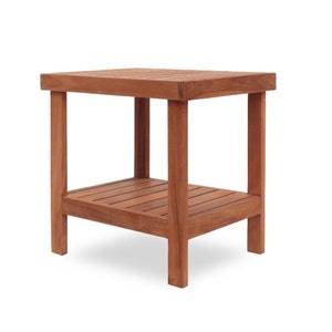 Könnte beinhalten: Ein quadratischer Beistelltisch mit zwei Ebenen aus rotbraunem Holz. Der Tisch hat eine Lattenoberfläche und ein unteres Regal, das von vier stabilen Beinen getragen wird. Das Design ist einfach und funktional, geeignet für den Innen- oder Außenbereich. Ca. 45 cm x 45 cm.