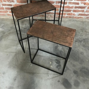Könnte beinhalten: Drei verschachtelte Tische mit schwarzen Metallrahmen und braunen Metallplatten. Die Tische sind versetzt angeordnet.