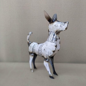 Könnte beinhalten: Metallhund-Skulptur, hergestellt aus recycelten Materialien. Der Hund ist weiß mit schwarzen Akzenten und weist einen industriellen Stil auf. Sichtbare Schweißnähte und Text auf der Oberfläche verleihen ihm einen einzigartigen Charakter. Ein dekoratives Objekt.