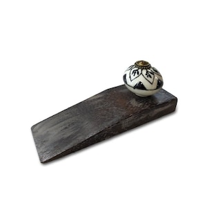 Könnte beinhalten: Ein Holz-Türstopper mit einem schwarzen und weißen Keramik-Knopf. Der Knopf hat ein Blumenmuster.