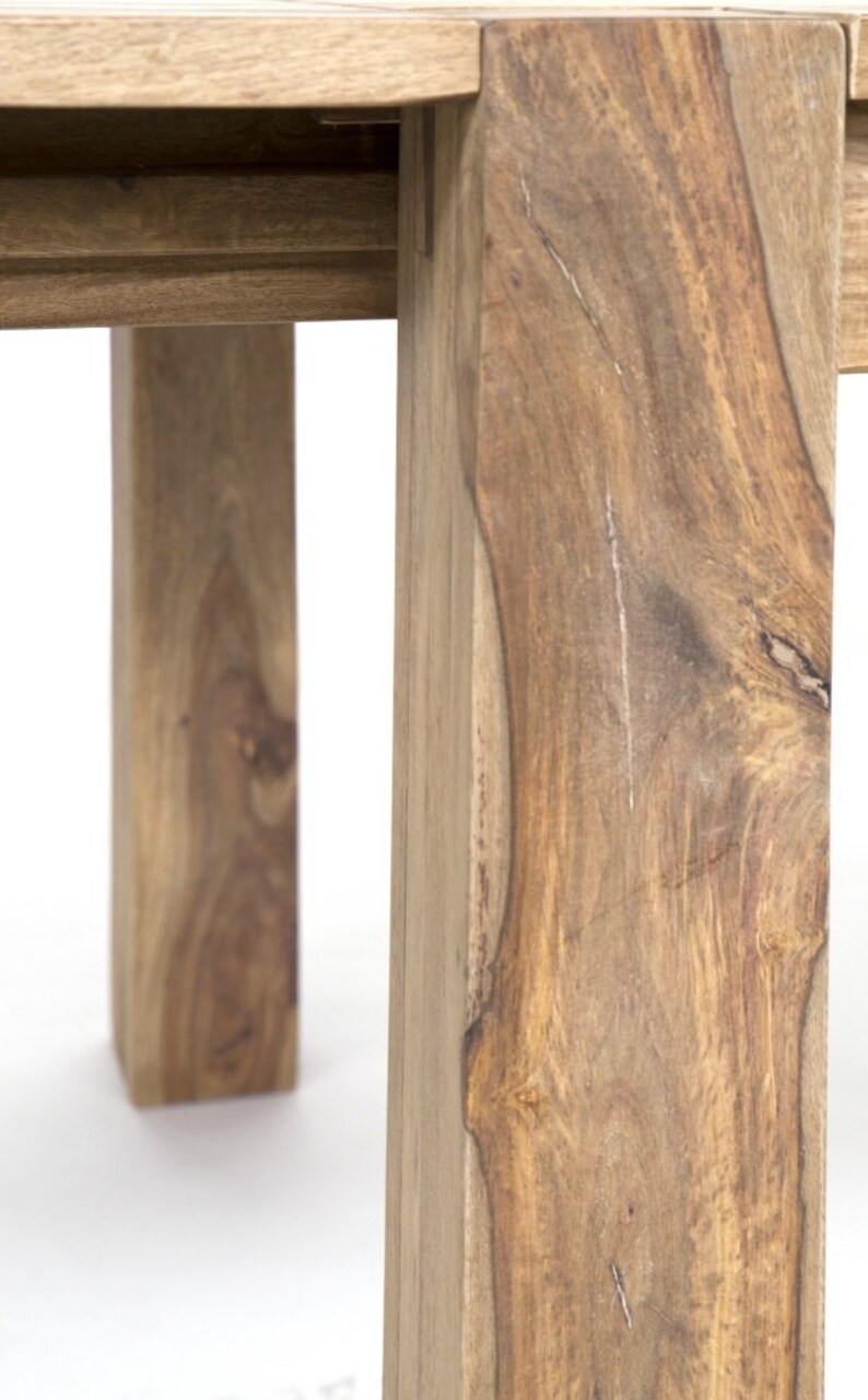 May include: Close-up of a wooden table leg, showcasing the natural grain and texture of the wood. The leg is a warm brown color, with visible knots and variations in the wood grain. The table appears to be sturdy and well-crafted.