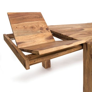 May include: A wooden dining table with an extending leaf. The table is made of light brown wood with visible grain. The extending leaf is partially open, revealing the mechanism. The table has a rectangular shape and a sturdy base.