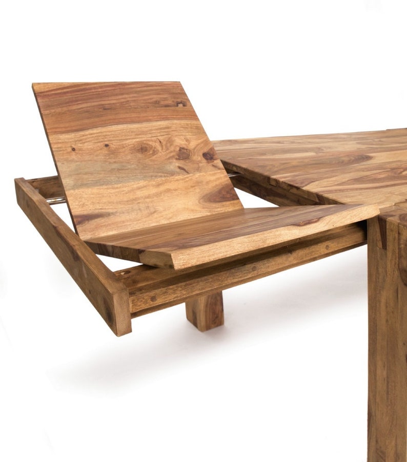 May include: A wooden dining table with an extending leaf. The table is made of light brown wood with visible grain. The extending leaf is partially open, revealing the mechanism. The table has a rectangular shape and a sturdy base.