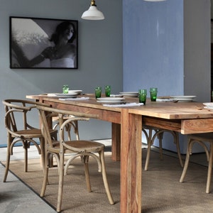 May include: A dining room scene featuring a large wooden table set with white plates and green glasses. Curved-back wooden chairs surround the table, and a framed black and white photograph hangs on the wall. Two pendant lights hang above the table.