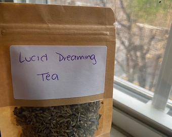 May include: A brown paper bag with a clear window showing dried lavender flowers. The bag has a white label with the handwritten text "Lucid Dreaming Tea".