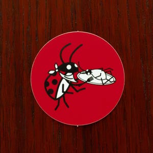 May include: A red circle sticker with a black and white illustration of a ladybug carrying a plate of food. The ladybug has a red body with black spots and a white face.