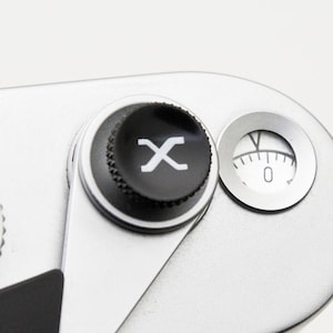 May include: Close-up of a silver camera with black dials and a white dial with numbers. The camera has a black button with a white "X" symbol and a small dial with a needle pointing to zero. The camera is labeled "LEICA CAMERA MADE IN GERMANY".