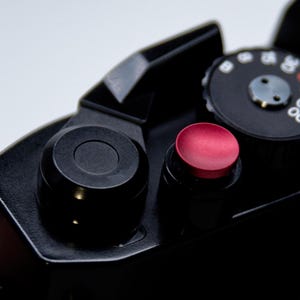 May include: Close-up of a black camera with a red button and a dial with the numbers 500, 250, and 125.