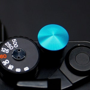 May include: A black camera with a blue knob and a dial with numbers 15, 18, 30, 60, 125, 250, and 500.