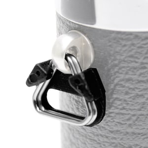 Può includere: Primo piano di una bottiglia termica grigia con una maniglia di trasporto nera. La maniglia è un anello triangolare con un anello di metallo.