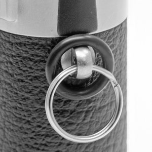 May include: A close-up of a black and silver keychain with a black rubber ring and a silver metal ring.