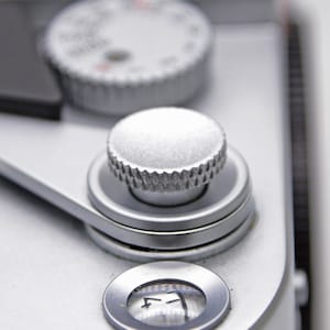 May include: Close-up of a silver camera with a silver knob and a small round window with the number "7" inside.