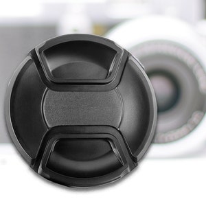 May include: A black lens cap with a textured surface and four tabs around the edge.