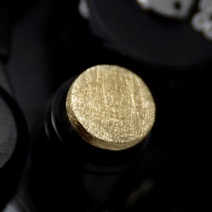Könnte beinhalten: Nahaufnahme einer schwarzen Kamera mit einem goldfarbenen Knopf. Der Knopf hat eine strukturierte Oberfläche.