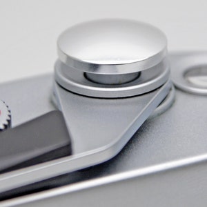 May include: A silver camera with a black lever and a silver knob with a number dial that reads "1, 2, 4, 8, 1000".