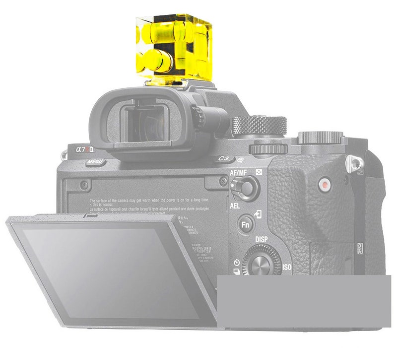 May include: A black digital camera with a bright yellow level attached to the top. The camera has a flip-out screen and various buttons and dials. The level is a clear, cube-shaped device with yellow liquid inside.