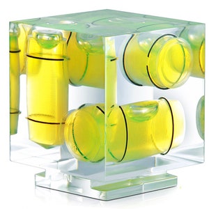 May include: A transparent, cube-shaped spirit level featuring multiple yellow and black bubble vials. The vials contain a bright yellow liquid. The level is designed for measuring horizontal and vertical alignment. Metric measurements.