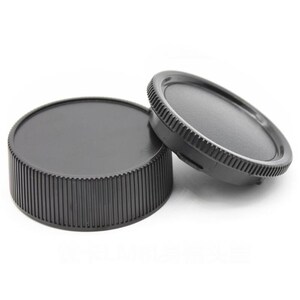 Può includere: Due tappi per obiettivo in plastica nera per una fotocamera. I tappi hanno un bordo scanalato e una parte superiore liscia.