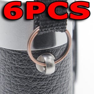 Może przedstawiać: Zbliżenie czarnego, teksturowanego przedmiotu ze srebrnym metalowym pierścieniem i czarnym paskiem. Czerwony tekst "6PCS" znajduje się na górze. Pierścień jest przymocowany do przedmiotu za pomocą srebrnego metalowego elementu.