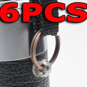 Może przedstawiać: Zbliżenie na termos ze stali nierdzewnej z czarnym paskiem i miedzianym pierścieniem. Tekst "6PCS" jest wyświetlany dużymi czerwonymi literami u góry obrazu.