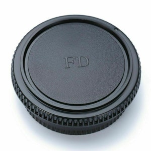 May include: Black camera lens cap with a textured surface and the letters "FD" embossed on the top.