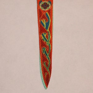 May include: A red, green, and blue woven fabric bookmark with a Celtic knot design.