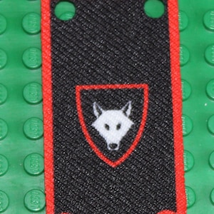 Könnte beinhalten: Schwarzer und roter Stoffumhang mit einem weißen Wolfskopf-Emblem auf einem Schild.