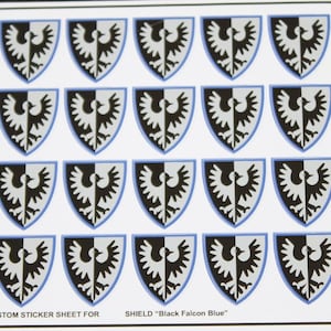 May include: A sheet of 18 black and white shield stickers with a blue outline. The shield features a black and white bird with a blue outline. The text "CUSTOM STICKER SHEET FOR SHIELD "Black Falcon Blue"" is at the bottom of the sheet.