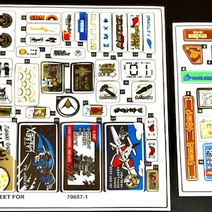 Può includere: Due fogli di adesivi per un set Lego Ninjago. Il primo foglio presenta una varietà di adesivi, tra cui un drago, un ninja e un edificio. Il secondo foglio contiene una mappa di Ninjago e un cartello che dice "Ninjago Tonight".
