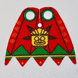 Könnte beinhalten: Roter und grüner LEGO Minifiguren-Umhang mit gold-schwarzem Design. Der Umhang zeigt ein stilisiertes Gesicht mit einer Krone und einem Sonnenstrahlenmuster.