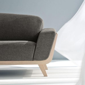 May include: A grey fabric sofa with a wooden frame and legs. The sofa has a curved back and a rounded armrest.