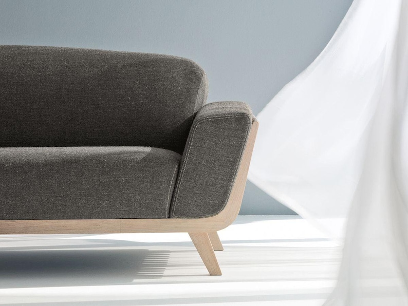 May include: A grey fabric sofa with a wooden frame and legs. The sofa has a curved back and a rounded armrest.