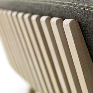 May include: Close-up of the back of a wooden chair with a grey fabric cushion. The chair has a slatted back with vertical wooden slats.