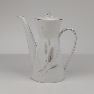 May include: White ceramic coffee pot with a silver trim and a wheat design. The pot has a lid and a handle.