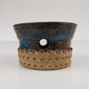 May include: A small, brown and blue ceramic planter with a textured base and a hole in the center.