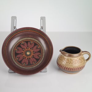 May include: A brown and cream ceramic creamer with a floral design and a brown and cream ceramic plate with a floral design.