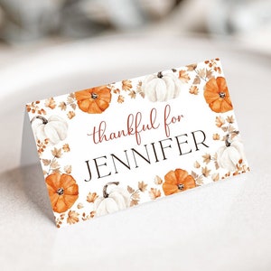 May include: A white card with a fall-themed border of orange pumpkins and white pumpkins with brown leaves. The text on the card reads "thankful for JENNIFER".